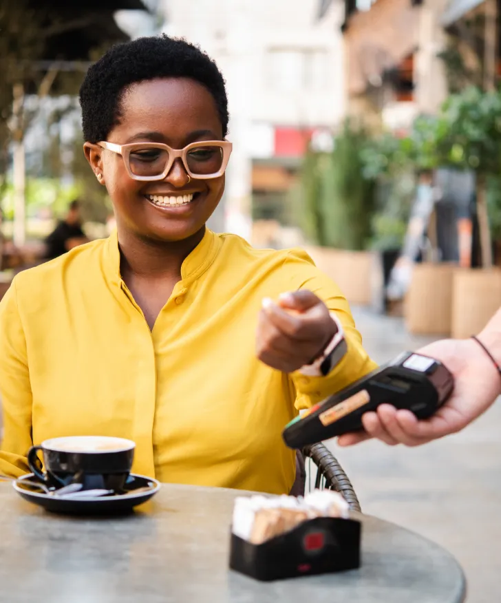 Customer tapping a bank card on a portable reader at a cafe table