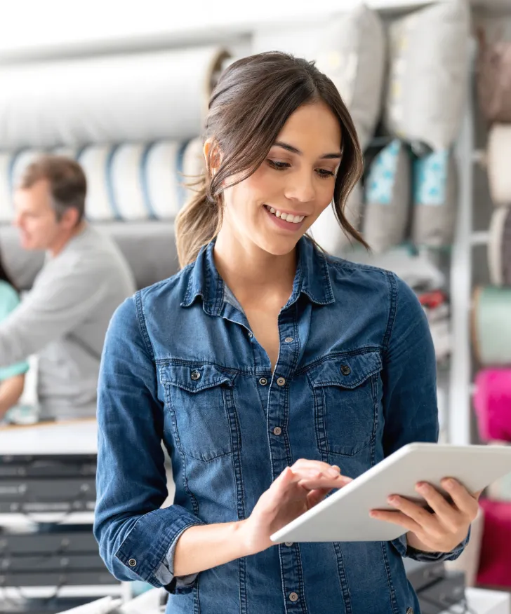 Shop assistant updating stock on a tablet beside a clothing rail